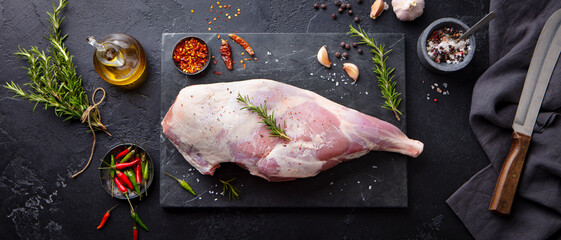 Raw lamb leg with spices and herbs on marble cutting board. Dark background. Top view.