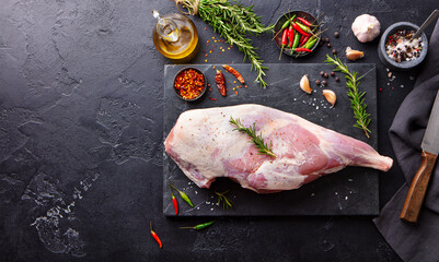 Raw lamb leg with spices and herbs on marble cutting board. Dark background. Copy space. Top view. © annapustynnikova