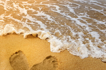 natural background. left footprints in the yellow sand. beach holiday. summer season, daytime. warm sunlight falls on the coast with a wave