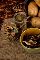 barley, spices in glass jars next to dried mushrooms and raw potatoes on a wooden brown table