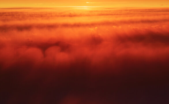 Abstract image. The setting sun beautifully painted fluffy clouds in red, orange, yellow in the evening sky. Close-up colorful striped smoky cloudy landscape in the sky. Puffs of red smoke.