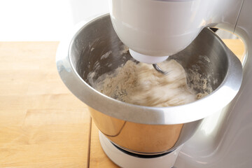 Stand mixer in action is stirring dough with the dough hook in a stainless steel bowl on a wooden kitchen workspace, motion blur, copy space