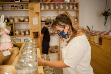 Caucasian woman in local store using mask and mantaining social distance bying daily products.