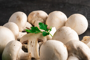 Champignon mushrooms healthy food on black plate with parsley greenery on dark black textured background, angle view macro