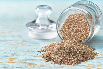 chia seeds are poured from a glass jar on a rustic table.  chia seeds in an open glass jar.