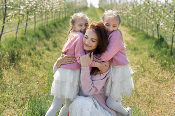 Portrait of a mother and her twin daughters in a blooming Apple orchard. Girls hug their mother
