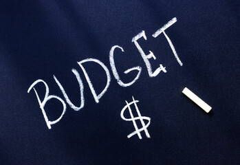 the word budget is written in white chalk on a black surface and a dollar sign