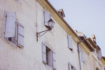Medieval building with outdoor lamp filtered. Facade of old house with window shutters. Ancient architecture concept. Historic building in village, France. Vintage house with street lantern.