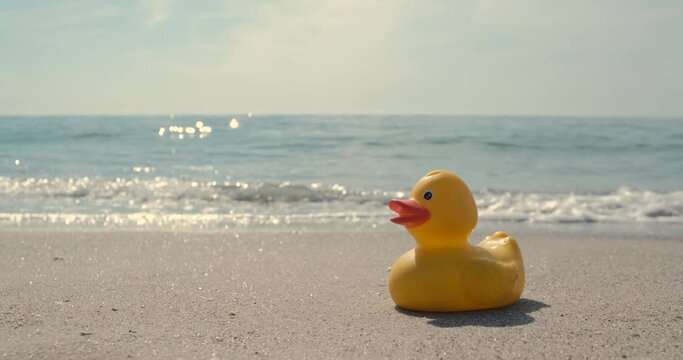 The yellow rubber duck went on vacation to the beach, the sea wave easily touches the duck.