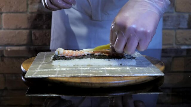 The process of rice rolls, sushi maki cooking. Roll contains rice, nori, mango and shrimp. Delicious food. Chef cook is wearing gloves. 