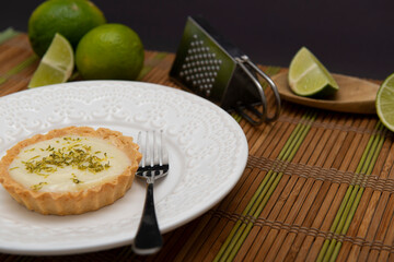 Side view of lemon tart on dish plate with lemon slices on table.