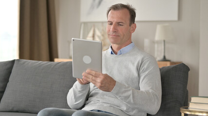 Cheerful Middle Aged Businessman using Tablet on Sofa