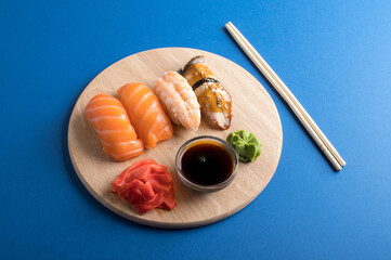 Delicious appetizing nigiri sushi set served on wooden plates with soy sauce and chopsticks. Flat lay on blue background