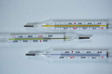 Three classic mercury thermometers with a scale of degrees Celsius lie on a clean white background. Concept of recovery from infection and coronavirus.