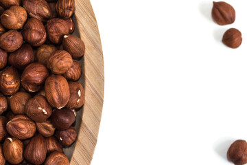 Hazelnuts in a bowl to the left and three hazelnuts outside on a white background
