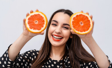 Happy young woman holding grapefruit halves near face. Cheerful smile with red lips.