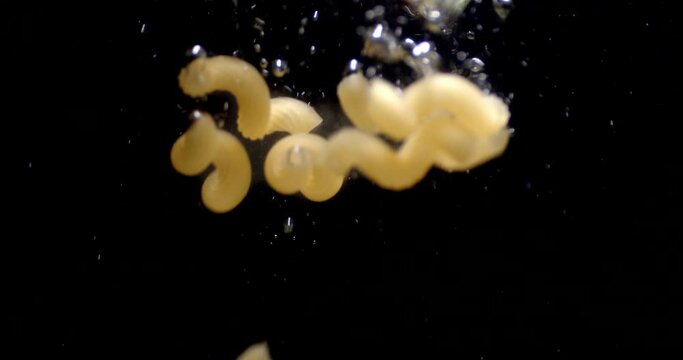 Cavatappi dry pasta falls under water with air bubbles.