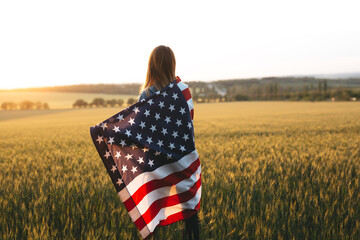 Beautiful girl with the American flag in a wheat field at sunset. 4th of July.  Independence Day.