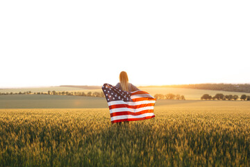 Beautiful girl with the American flag in a wheat field at sunset. 4th of July.  Independence Day.