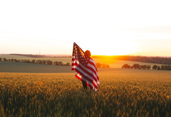 Beautiful girl with the American flag in a wheat field at sunset. 4th of July.  Independence Day. - Powered by Adobe