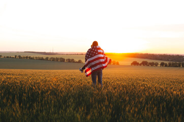 Naklejka na ściany i meble Image of young couple with the American flag in a wheat field at sunset. Independence Day, 4th of July.