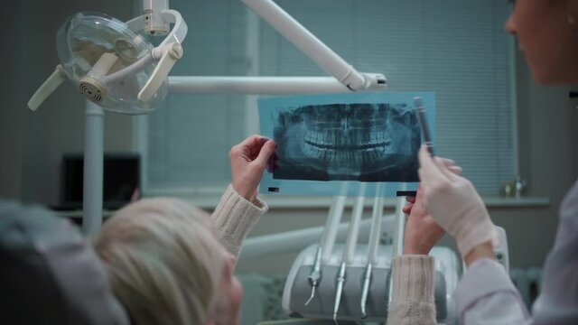 professional dentist female show panoramic mouth x-ray image to patient