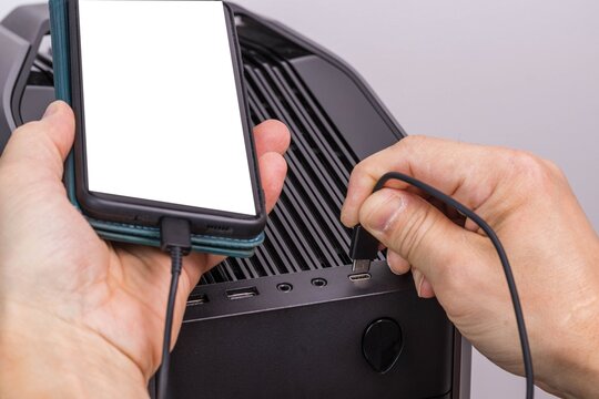 Close up view of man hand connecting usb cable  mobile phone with mockup image blank screens to black computer. 