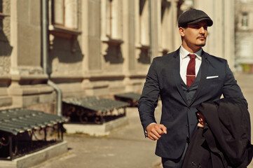 Portrait of retro 1920s english arabian business man wearing dark suit, tie and flat cap walking on...