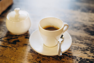 Aromatic fresh coffee in a white cup. Americano with sugar bowl on table in cafe. Americano in a small white cup.