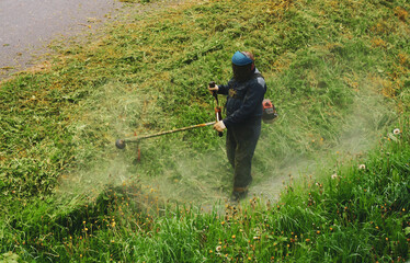 A man mows grass with a gasoline scythe in a protective uniform