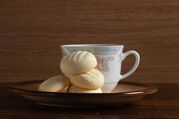 Small round cookies and Cup of coffee in brown dish on wooden table.