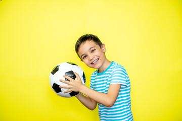 Fan sport boy player hold soccer ball in striped t-shirt celebrating happy smiling laughing show thumbs up success sign free text copy space isolated on yellow background. Looking at camera