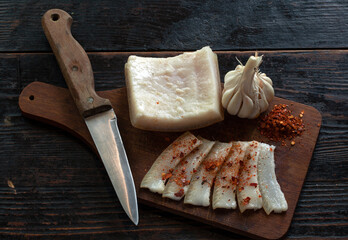 Slices of bacon sprinkled with paprika and a head of garlic, served on a wooden board.