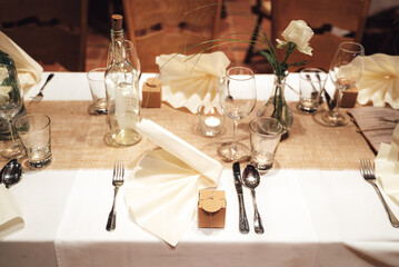 Elegant table setting with cutlery, napkin and glassware on white table cloth. Celebration, birthday and wedding concept.