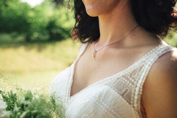 Brunette bride in white wedding dress neckline close up. Necklace on the neck. Outdoor photo,...