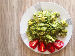 Fried green asparagus with scrambled eggs and tomato slices on a plate. Top view on wood texture table background