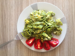 Fried green asparagus with scrambled eggs and tomato slices on a plate with a fork. Top view on wood texture table background