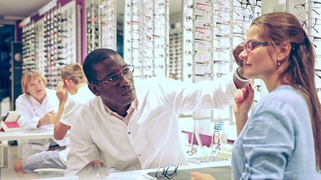 Professional male optician helping client to choose a spectacles  in medical shop