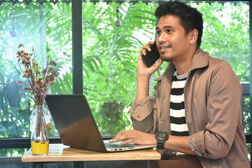 Handsome business man talking with customer by use to mobile phone and check mail on computer laptop between working.