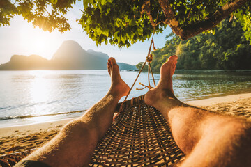 Feet of adult man relaxing in a hammock on the beach during summer holiday
