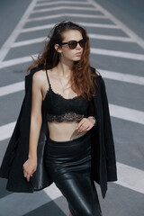 A model girl with a jacket on her shoulders and sunglasses, posing against the background of road markings.