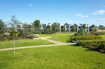 Obraz premium A public park with grass and footpath with some modern residential townhouses/Australian homes in the distance. Concept of suburban living, environment and real estate. Melbourne, Australia.