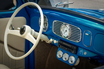 Part of the interior of blue old timer car with steering wheel, speedometer, oil, temperature dials, front panel