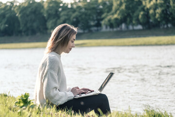 Blonde girl resting after working on a laptop on the grass by the river