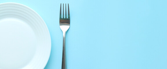 Part of a white flat empty plate and a silver metal fork on a blue background. Selective focus. Space for text. Serving. Copy space. Layout.Banner
