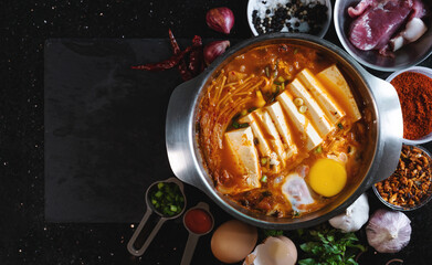 Traditional Korea food, Kimchi Jjigae soup with soft tofu and egg, surround with fresh ingredients. Top view with copy space