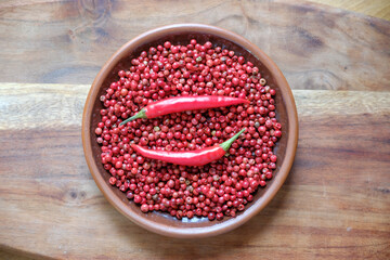 Pink peppercorns and red hot chili peppers in a clay plate standing on a wooden background.