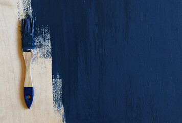 A paint-stained brush lies on a wooden surface, unpainted with dark blue paint . Selective focus....