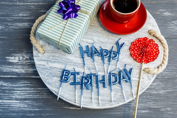Happy Birthday postcard on gray wooden table with cup of coffee, present and candles. Flat lay, top view 