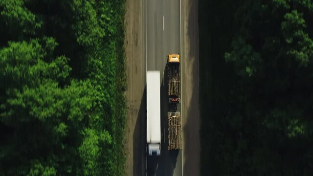 Double length log semi truck driving on straight highway / Freight truck haul timber across asphalt road. Aerial drone top down follow mid shot at summer sunset